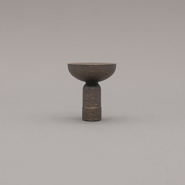 Skinny knurled knob in antique english finish standing upright on grey background. 