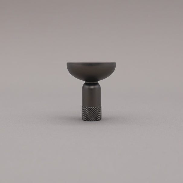 Upright view of skinny knurled knob in graphite finish on grey background.