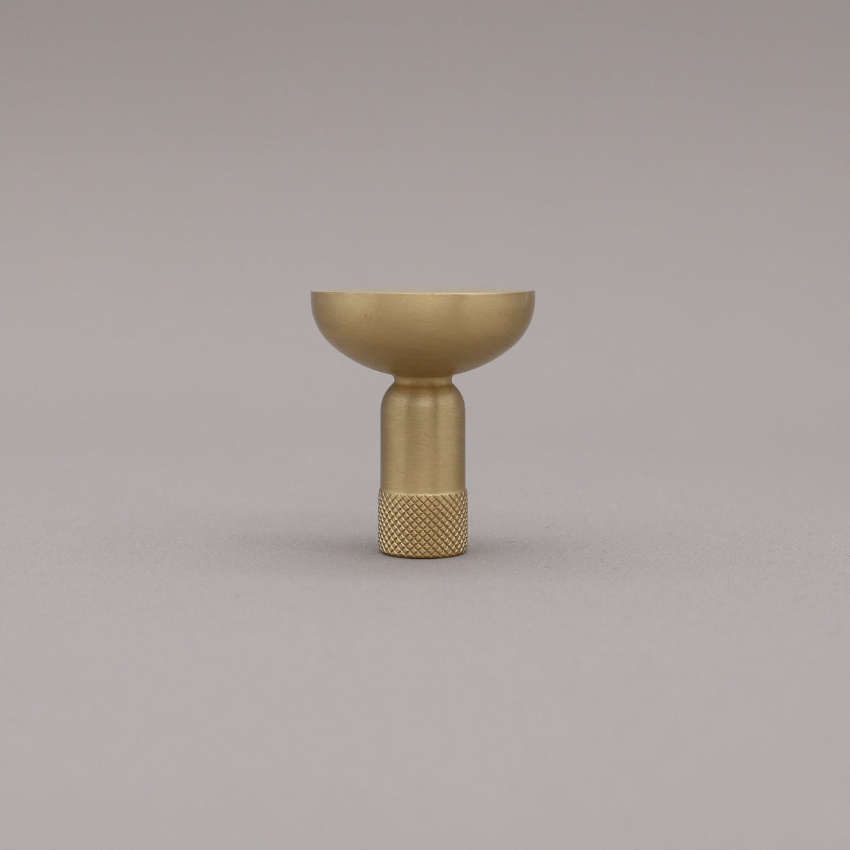Upright view of skinny knurled satin brass knob on grey background.