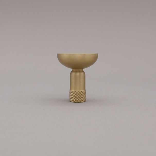 Upright view of skinny knurled satin brass knob on grey background.