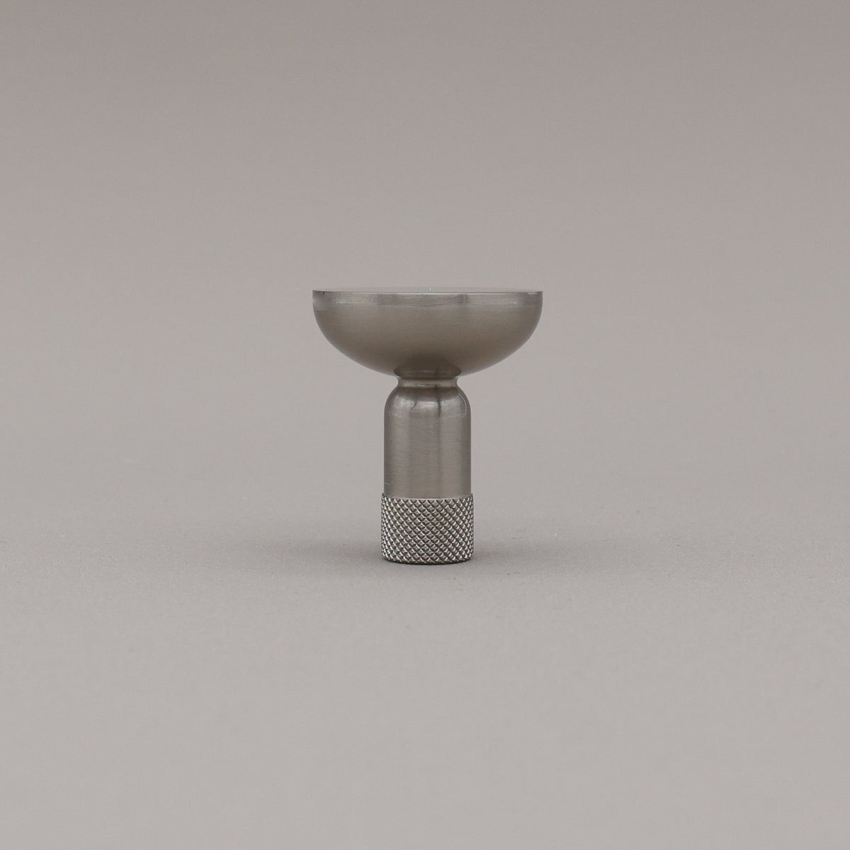 Skinny knurled knob in satin nickel finish standing upright on grey background. 
