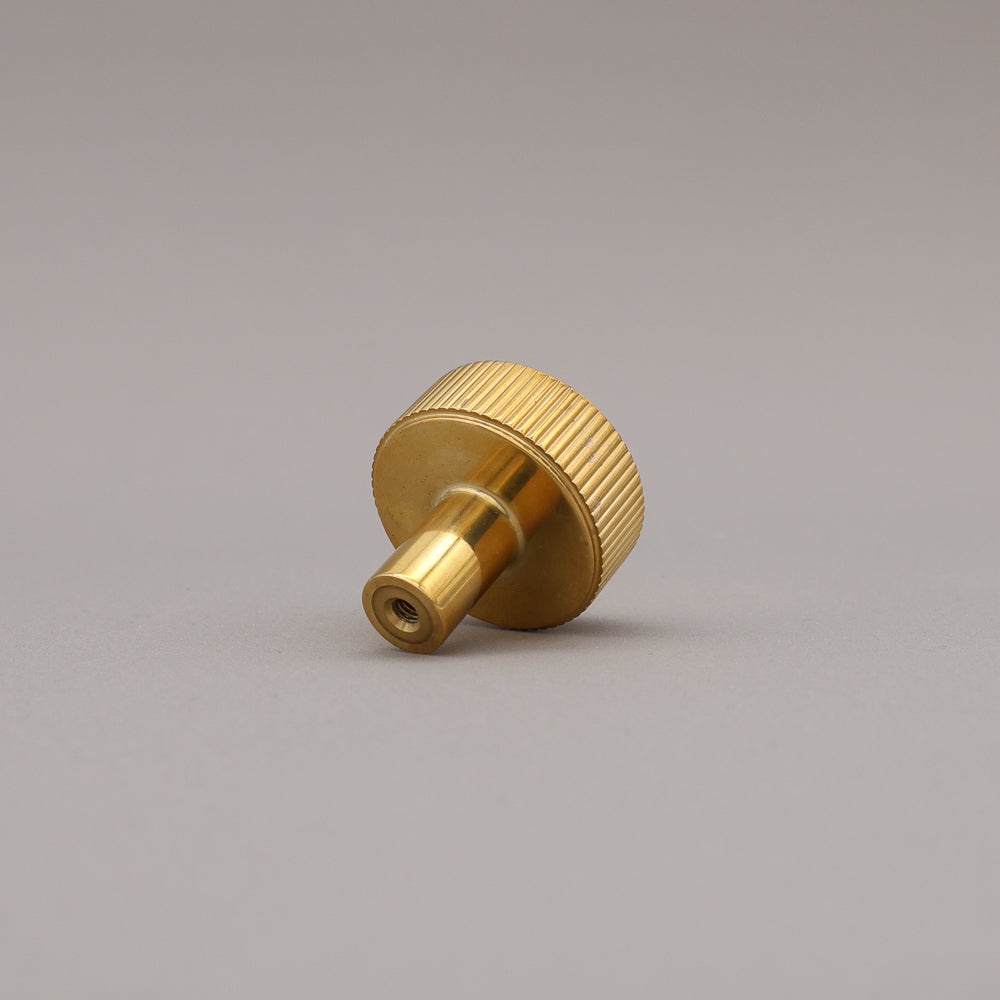 unlacquered polished brass gold textured ribbed knob with fluting detail on a gray background