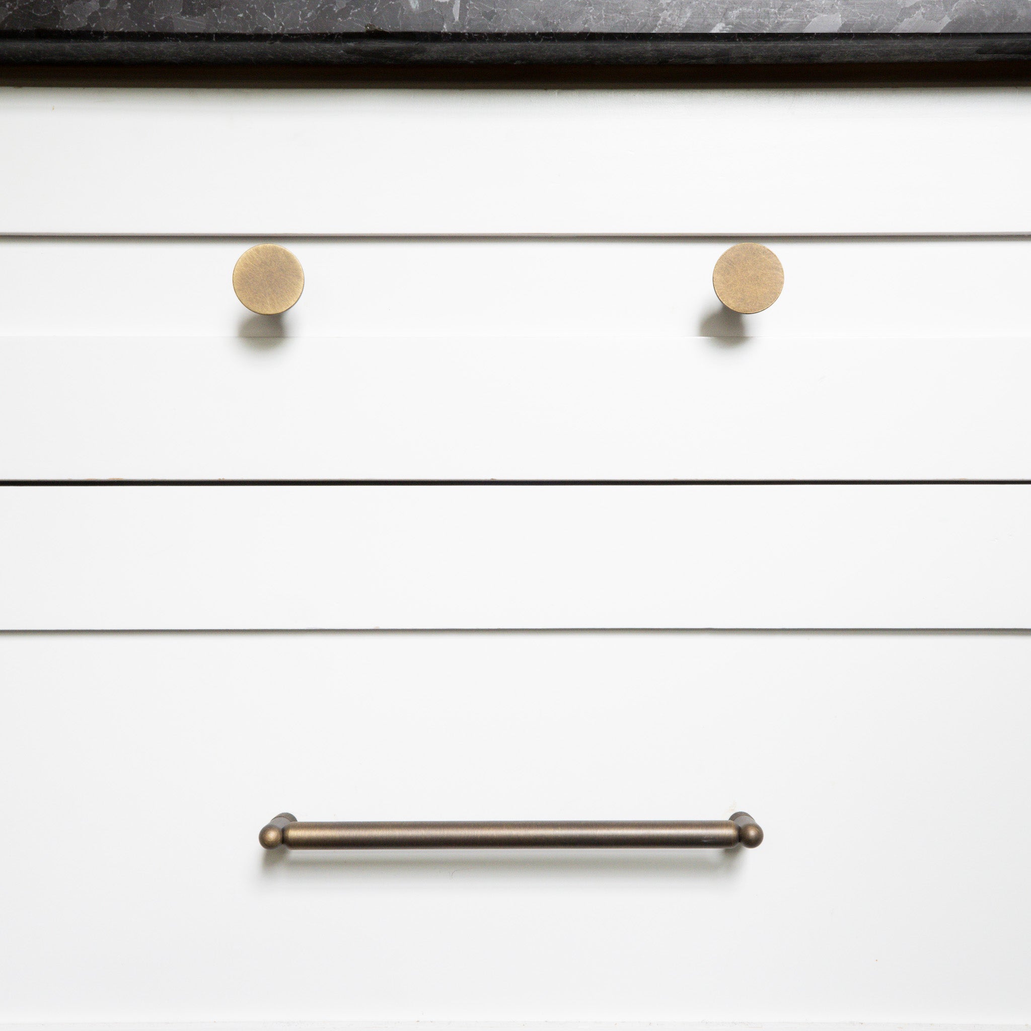 Close-up of white drawers with antique english knobs and an antique english handle.