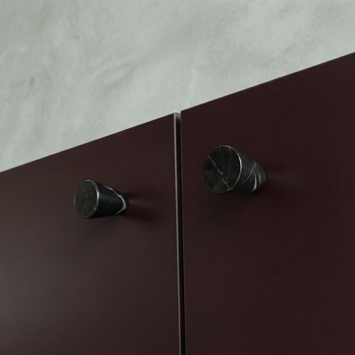 Marble knobs finished in a Black Marble on Burgundy cabinets.