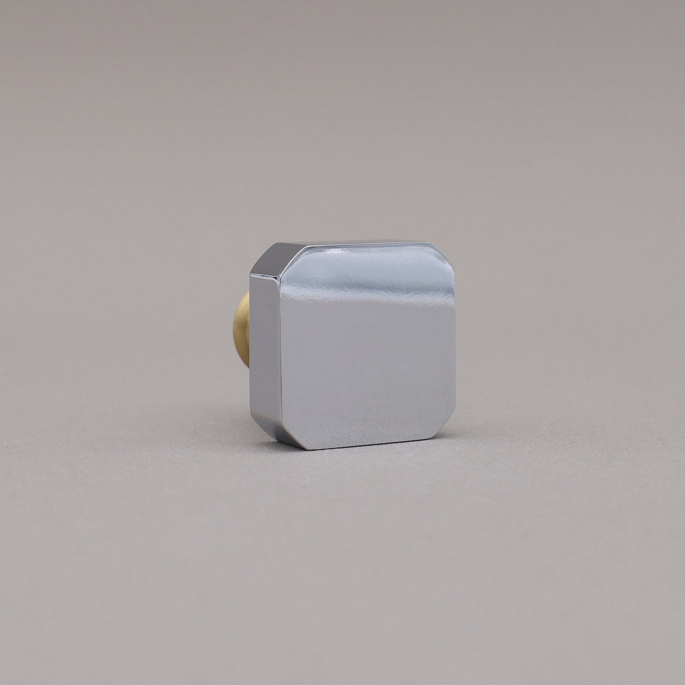 Polished chrome and brass gold square knob on a gray background