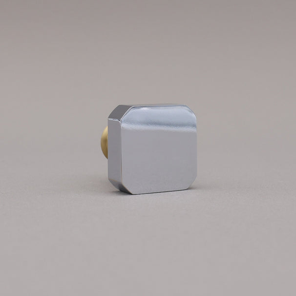 Polished chrome and brass gold square knob on a gray background