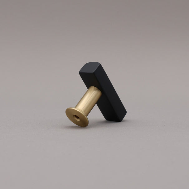Back Angled satin brass and black t-knob brass cabinet knob on gray background.