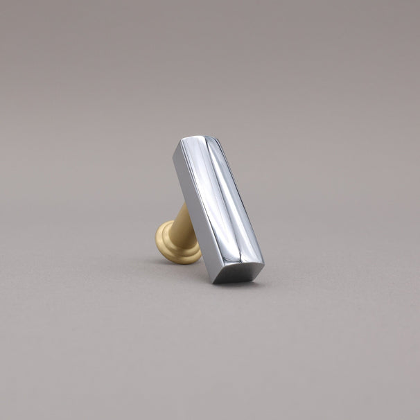 Leaning satin brass and polished chrome t-knob brass cabinet knob on gray background.