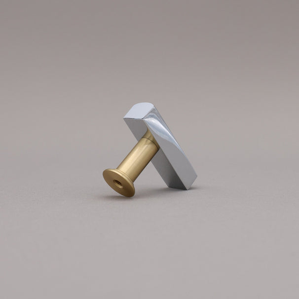 Back leaning satin brass and polished chrome t-knob brass cabinet knob on gray background.