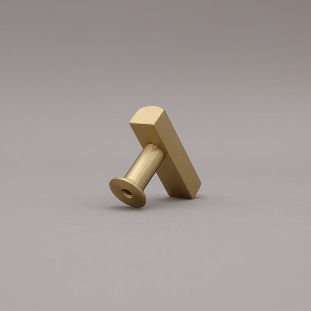 Diagonal leaning satin brass t-knob brass cabinet knob on gray background.