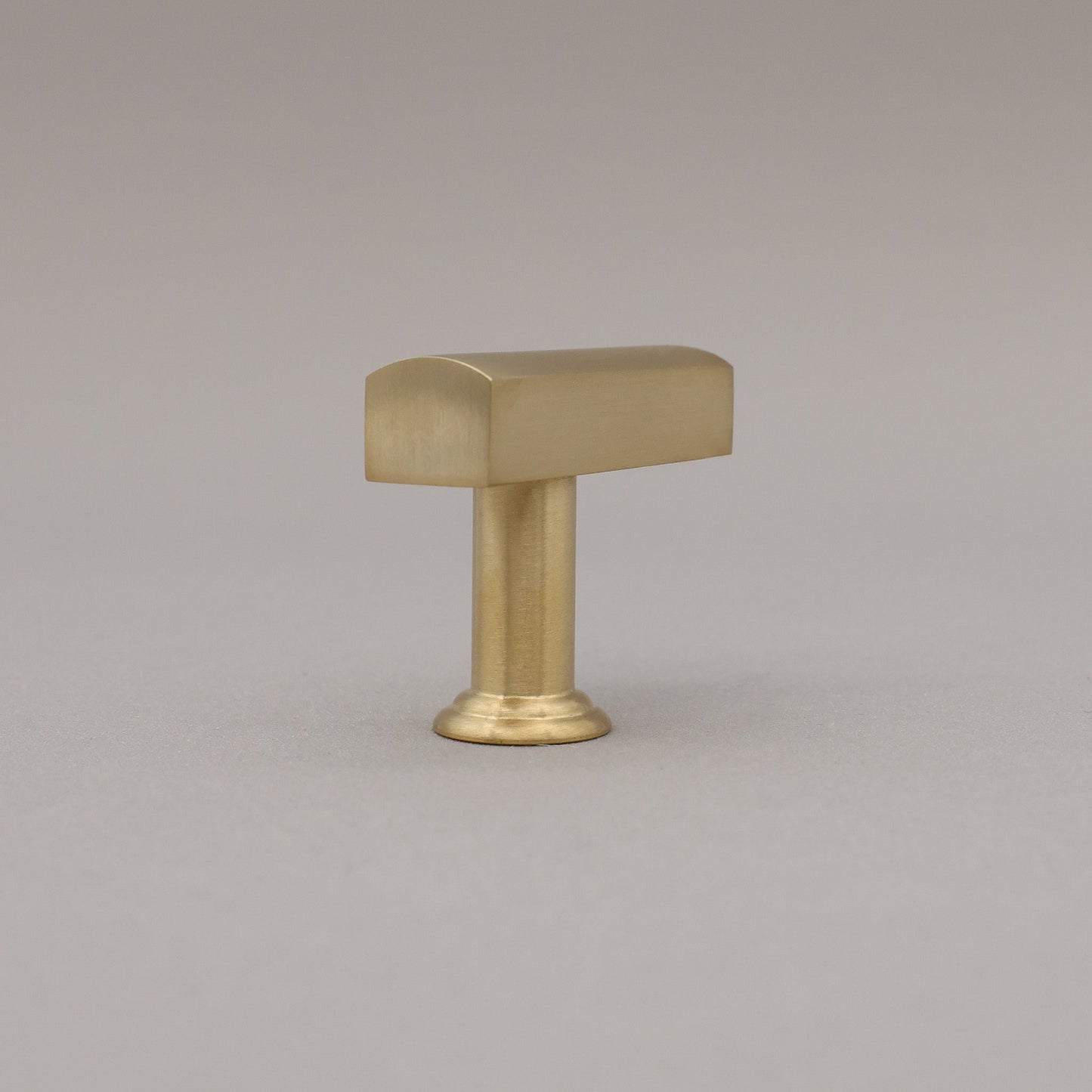 Unlacquered satin brass t-knob standing on a gray background rear view