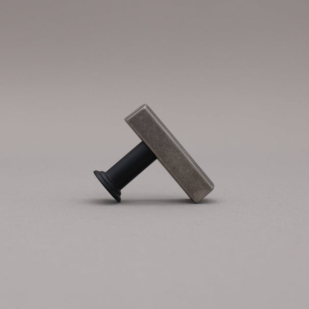 Leaning matte black and weathered nickel  t-knob brass cabinet knob on gray background.