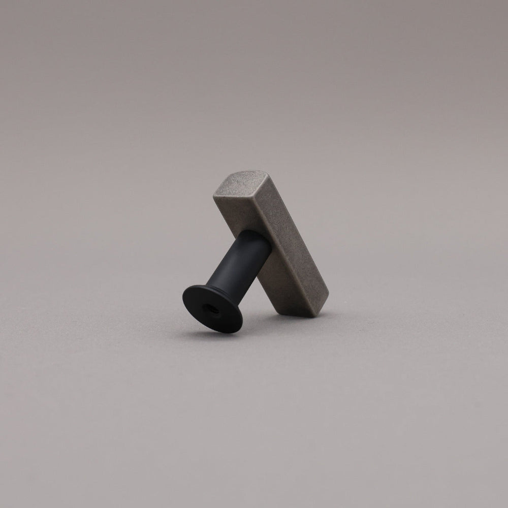 Back leaning matte black and weathered nickel  t-knob brass cabinet knob on gray background.