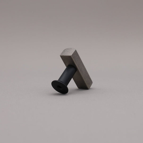 Back leaning matte black and weathered nickel  t-knob brass cabinet knob on gray background.