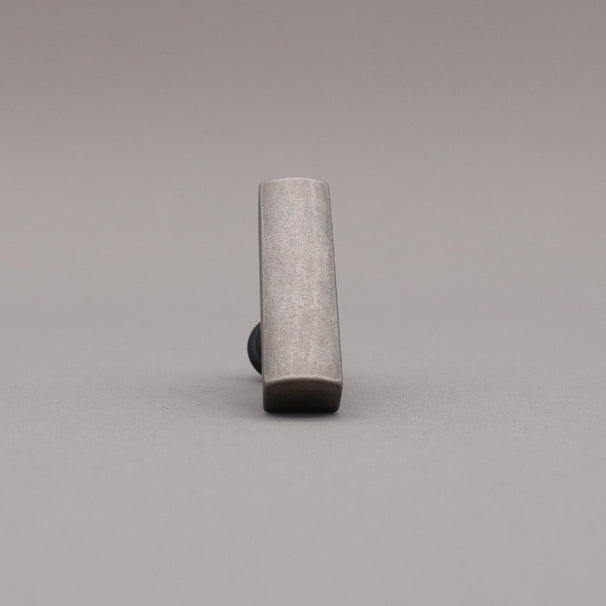 Front leaning matte black and weathered nickel  t-knob brass cabinet knob on gray background.