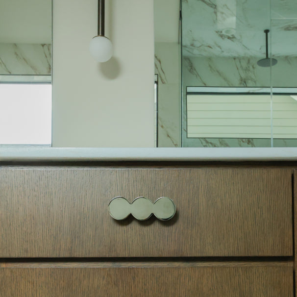 Statement circular cabinet pull in polished nickel mounted on a bathroom cabinet.