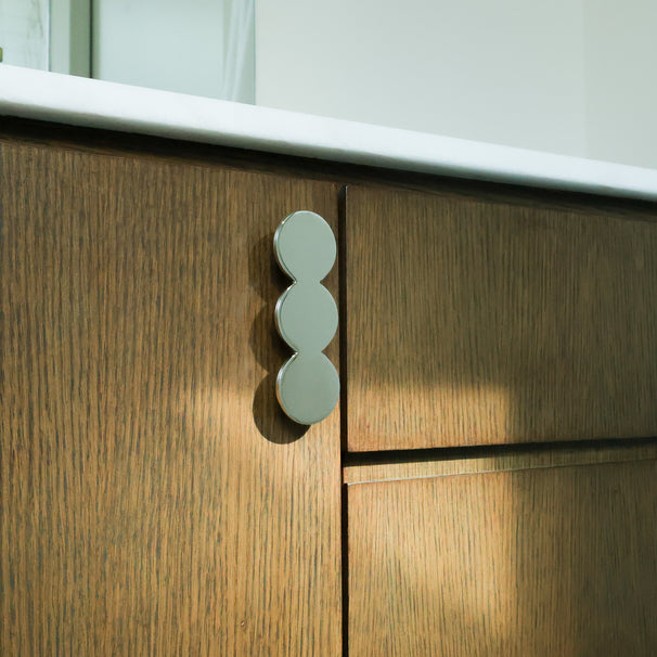 Statement circular cabinet pull in polished nickel mounted on a bathroom cabinet.