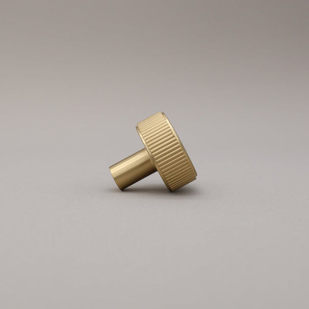 Profile view of satin brass knob on gray background.