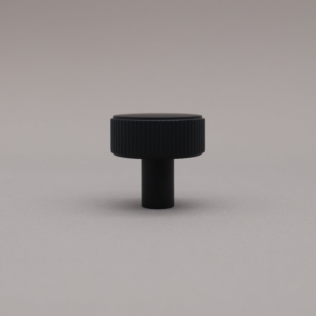Matte black ribbed knob on gray background standing upright.