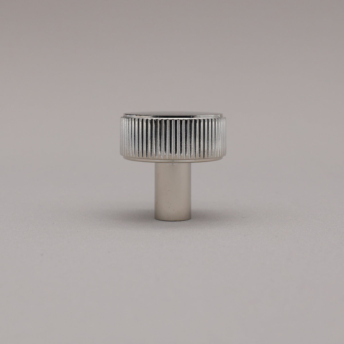 Polished nickel fluted ribbed knob on gray background standing upright.