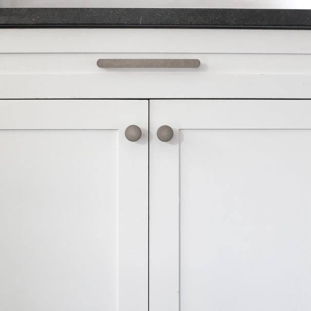 Ribbed knobs and pull on white kitchen cabinets with black counter.