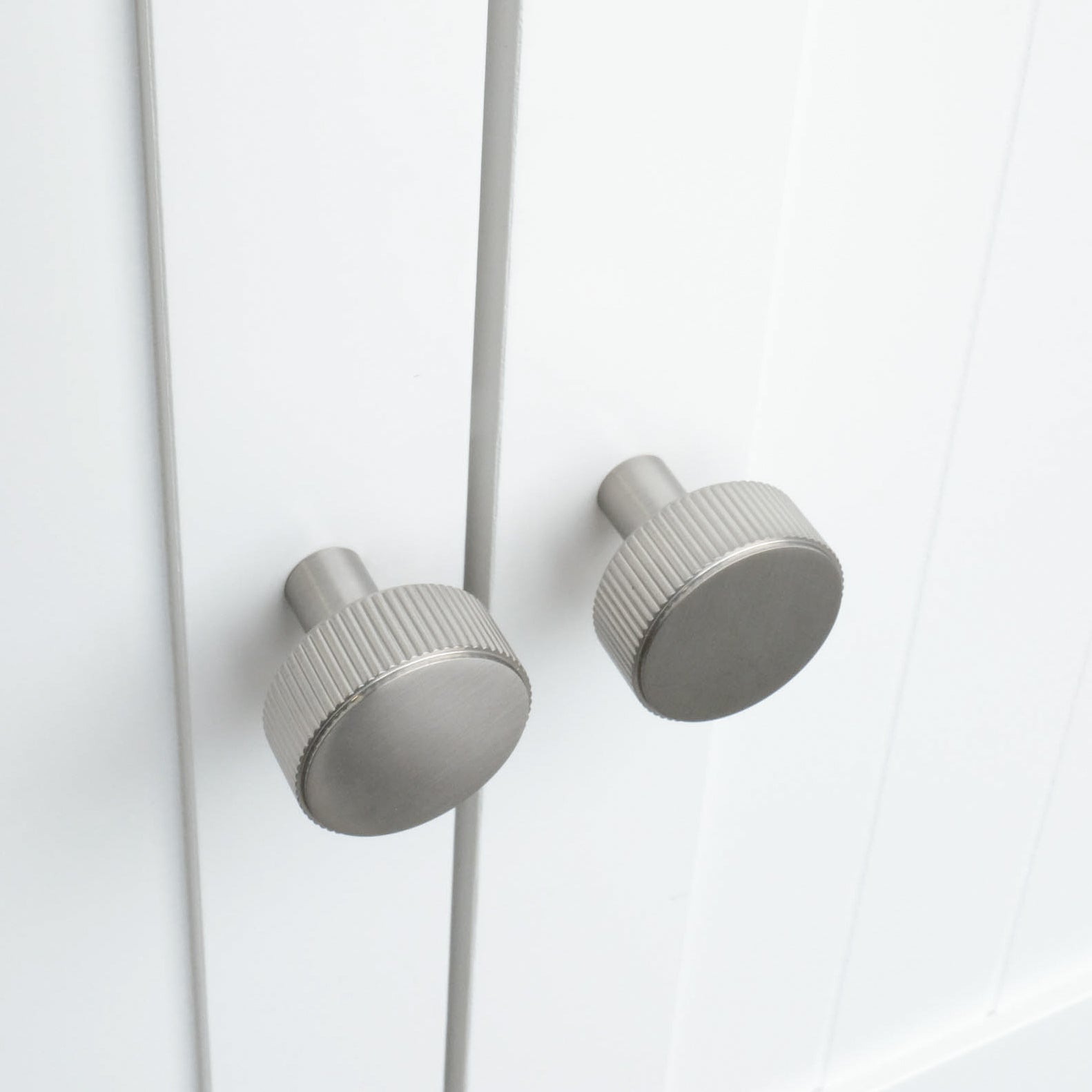 Two textured satin nickel knobs on white kitchen cabinets with ribbed exteriors. The knobs are round. 