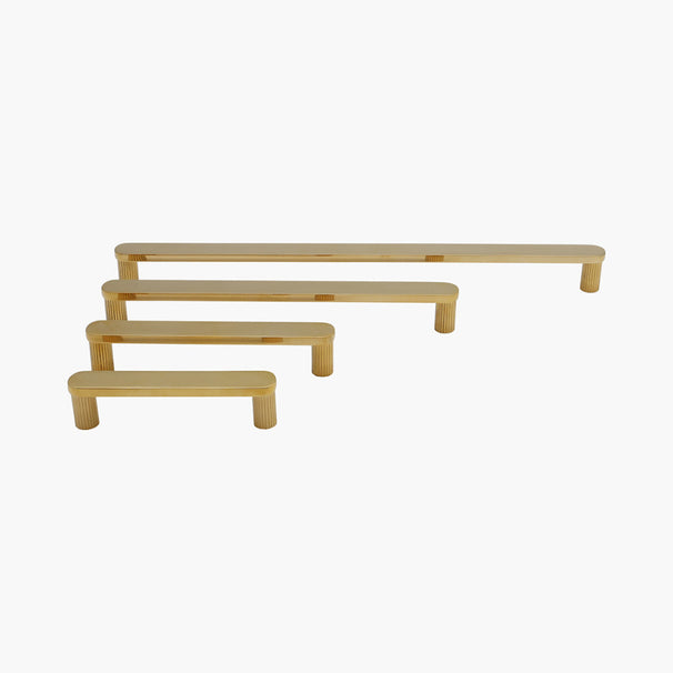 four ribbed cabinet pulls in unlacquered polished brass in four sizes on white background