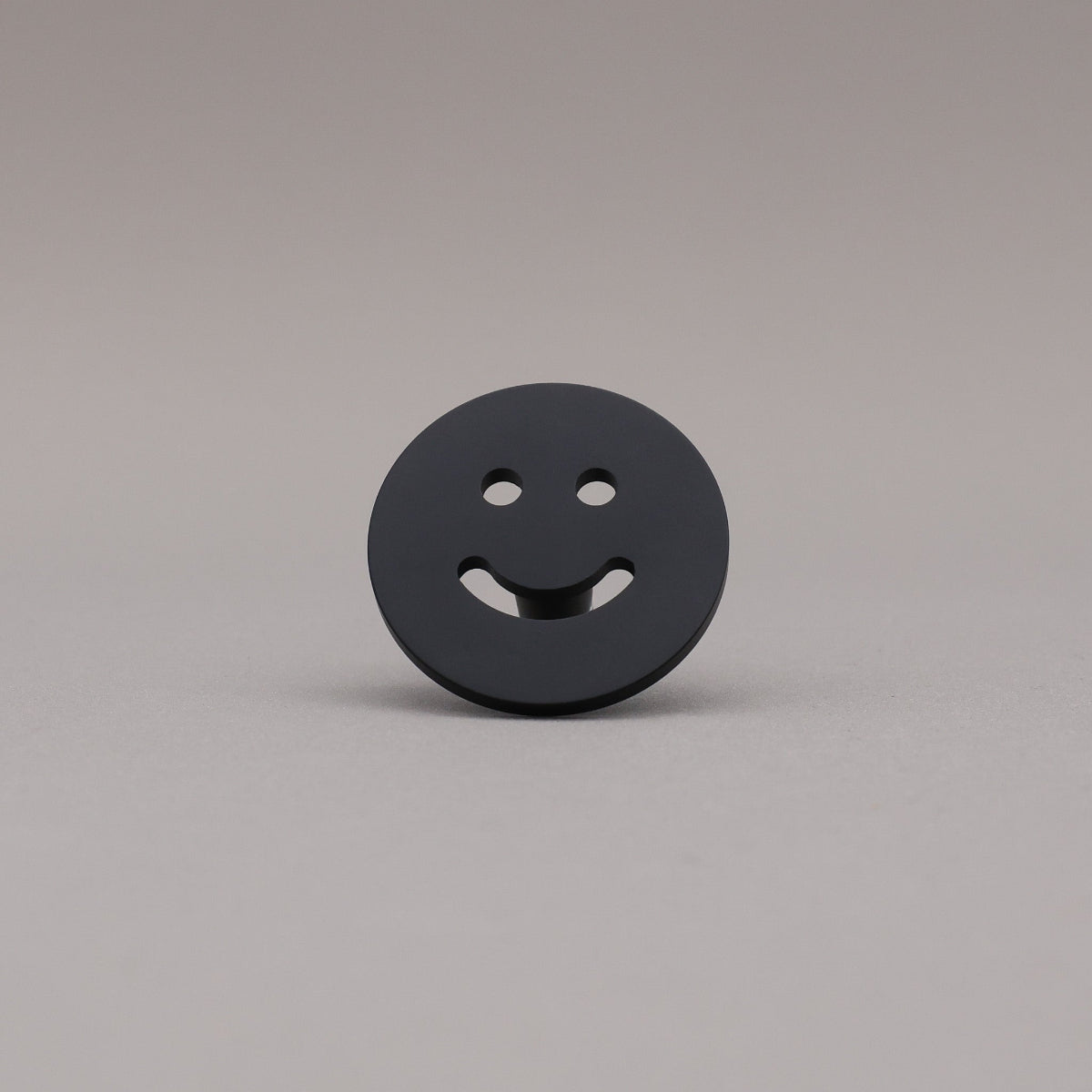 Smiley face knob finished in Matte Black on a gray background.