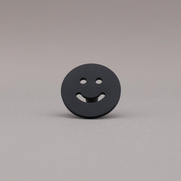 Smiley face knob finished in Matte Black on a gray background.