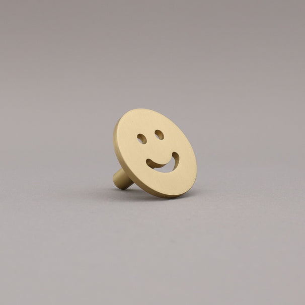 Satin brass smiley face object on a gray background