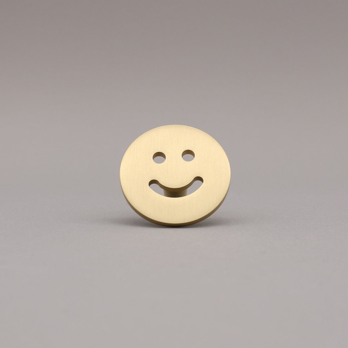 Satin brass smiley face knob button on a gray background.