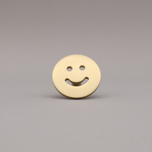 Satin brass smiley face knob button on a gray background.