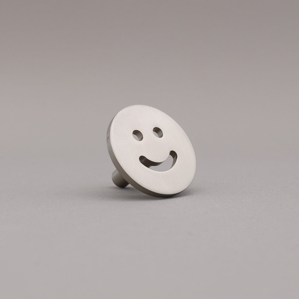 Smiley face knob on a gray background finished in satin nickel.