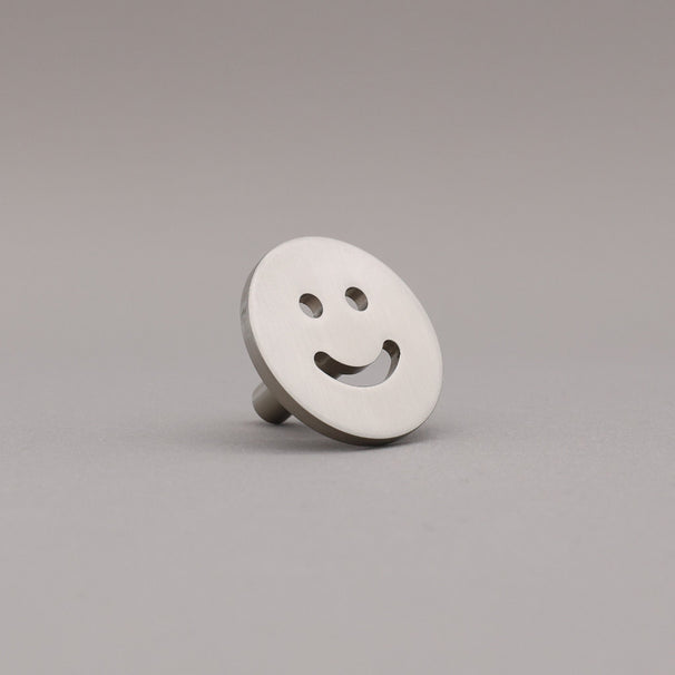 Smiley face knob on a gray background finished in satin nickel.