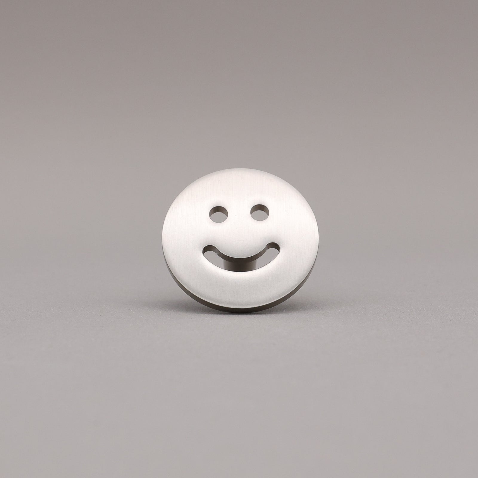 Smiley face knob finished in Satin Nickel on a gray background.