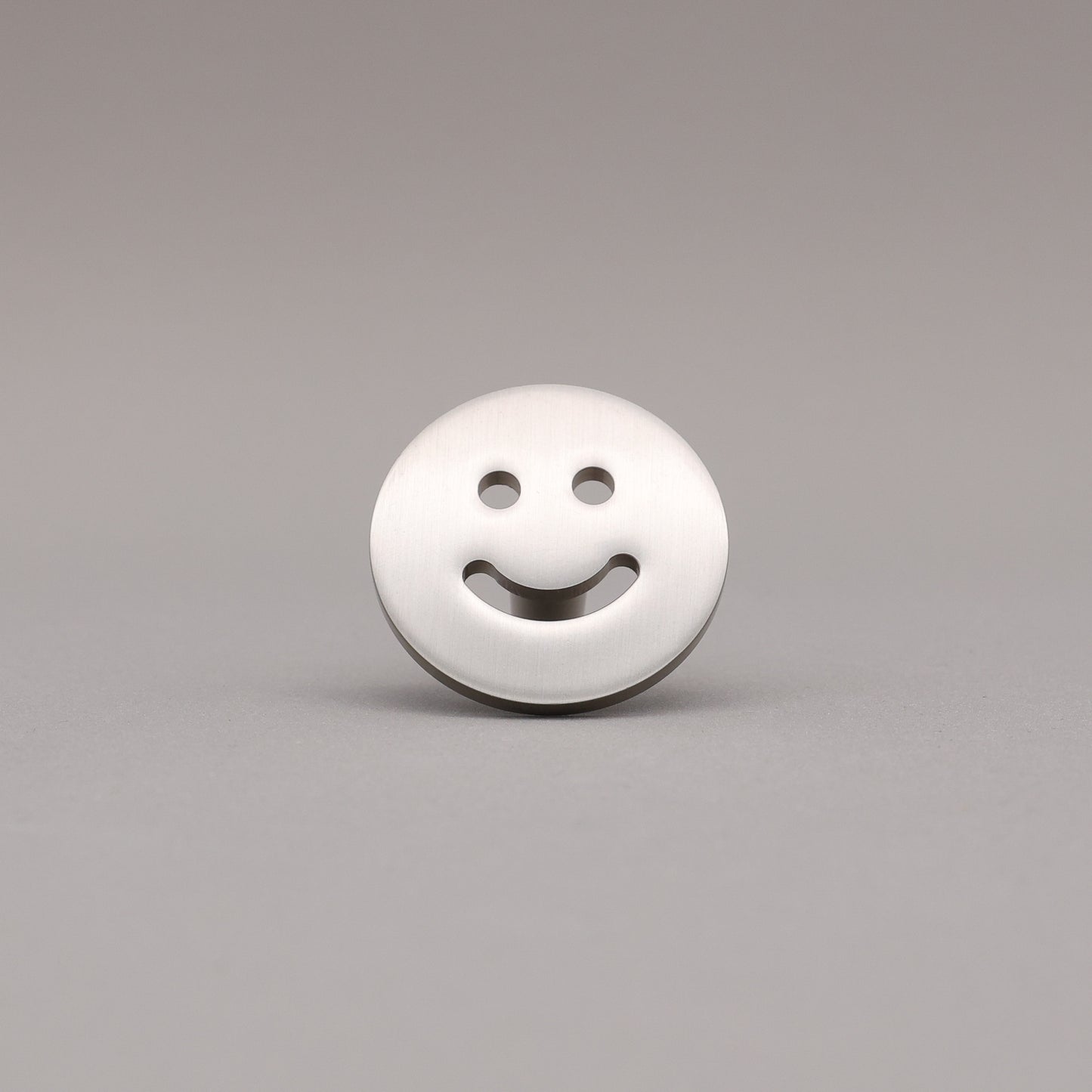 Smiley face knob finished in Satin Nickel on a gray background.