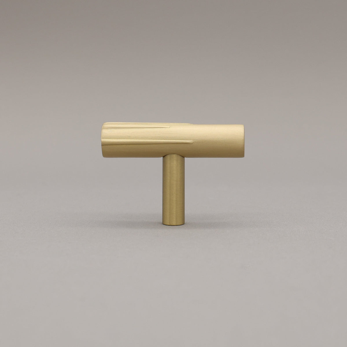 Sunburst t-knob made out of satin brass on a grey background.