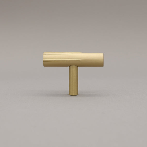 Sunburst t-knob made out of satin brass on a grey background.