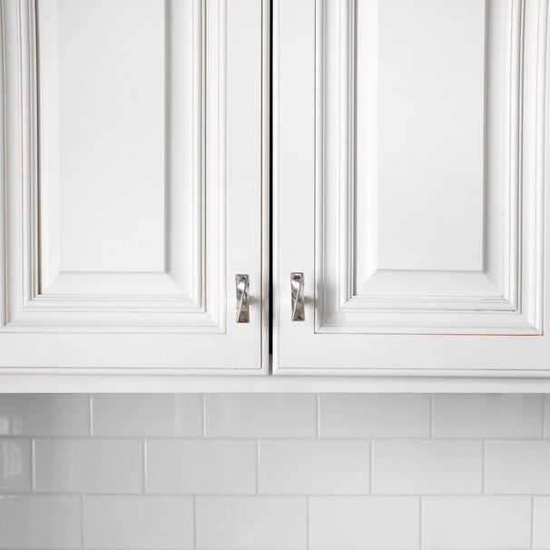 Close-up of white kitchen cabinets with polished nickel knobs against a white tiled backsplash.