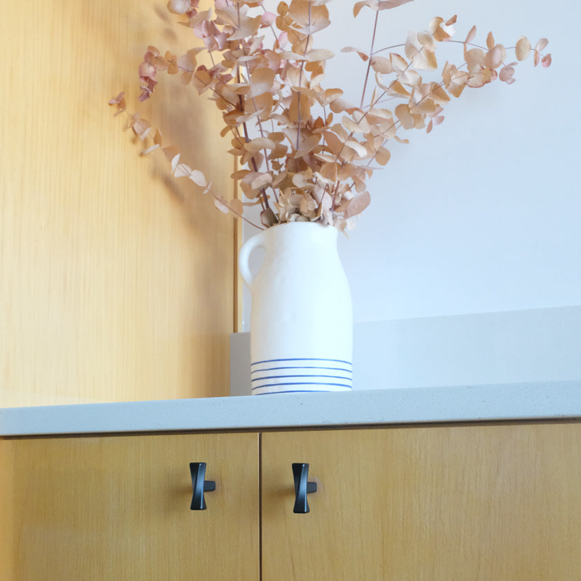 Two Black Twist Knobs on Wood Cabinets with White Vase and Eucalyptus