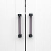 Two Clarity 96mm center to center cabinet pulls in Smoke Acrylic and Matte Black installed on white cabinet doors
