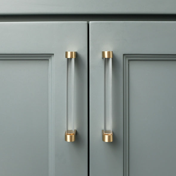 Two acrylic 5" center to center cabinet pulls in Clear Acrylic and Satin Brass installed on blue cabinet doors