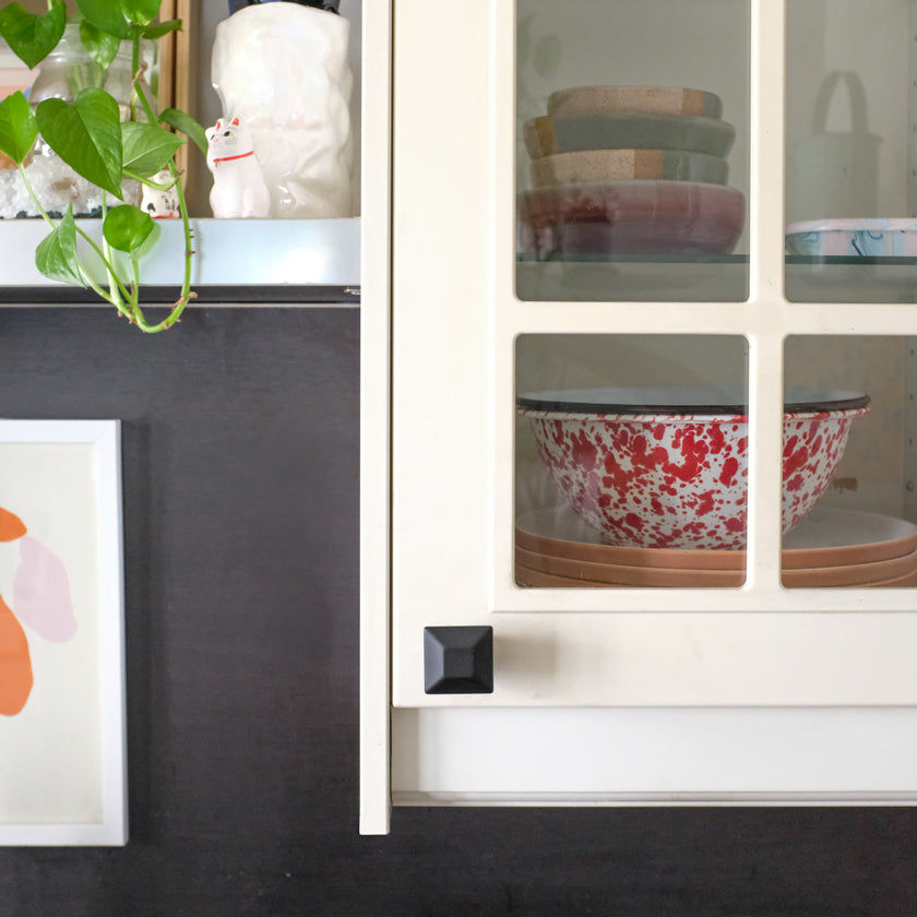 One Matte Black Diamond knob installed on a white cabinet door with glass panels