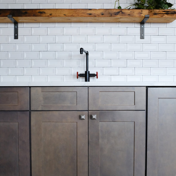 Two Weathered Nickel Diamond knobs installed on dark brown cabinets in a kitchen with white tiles and a black faucet