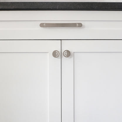 One 8" Hapny Horizon cabinet pull and two Horizon knobs in Satin Nickel installed on white cabinet doors and drawers