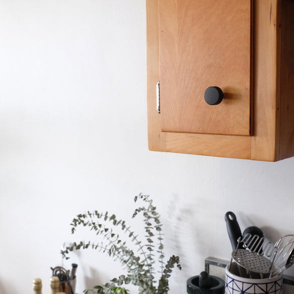 Matte Black Hapny Ribbed knob installed on a wood kitchen cabinet door