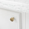 Hapny Ribbed knob in Satin Brass installed on a white cabinet door with marble countertop