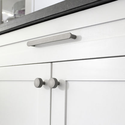 One Ribbed 8" pull and two cabinet knobs in Weathered Nickel installed on white cabinet doors with a black marble countertop