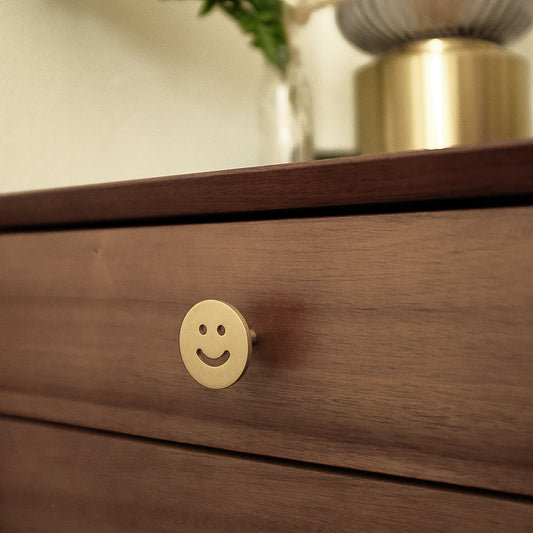 Two Satin Brass Smiley knobs, one standing and one front-facing while laying down