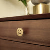 Close-up of Satin Brass Smiley Knob installed on a brown side-table drawer